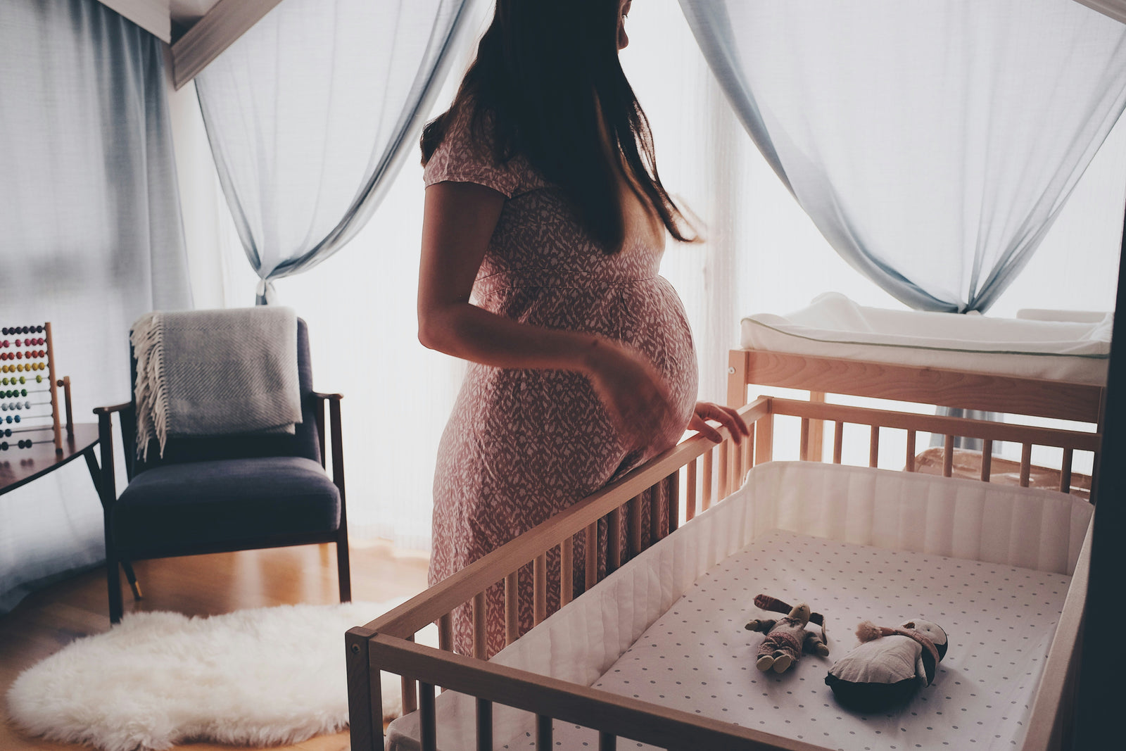 pregnant women with linen maternity dress standing close to toddler bed