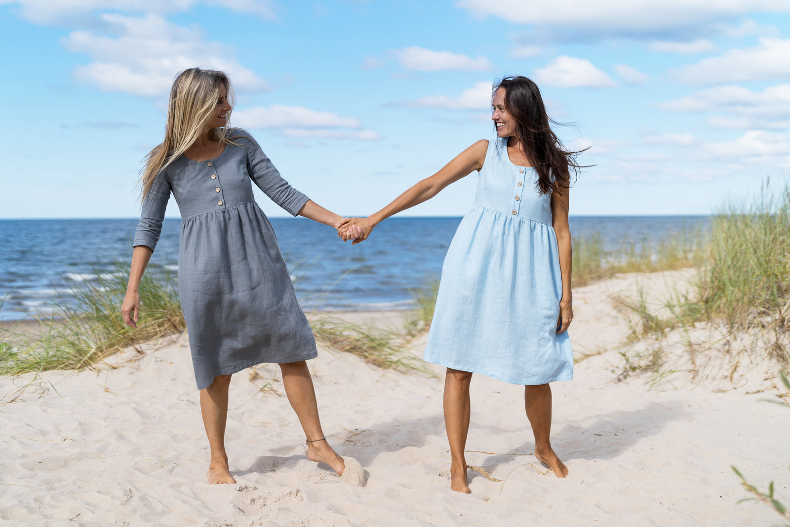 Girls dancing on the sand near sea with linen dresses