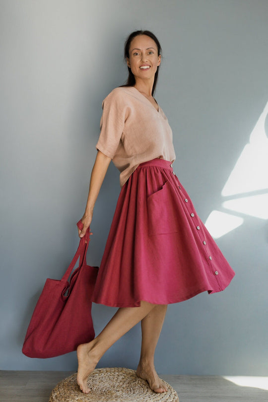 Women demonstrates Buttoned front linen skirt capri in raspberry color powder color top and raspberry color tote bag
